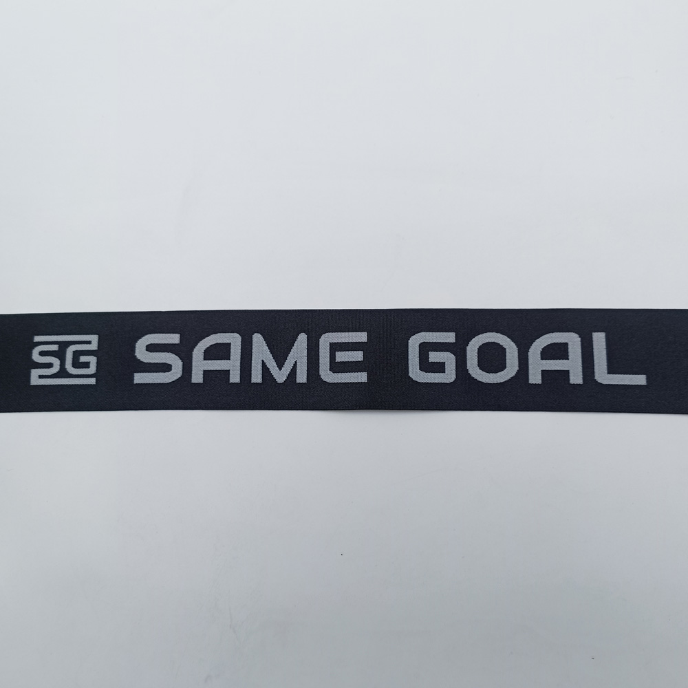 Flat view of a dark jacquard elastic band showing woven SG emblem and SAME GOAL lettering