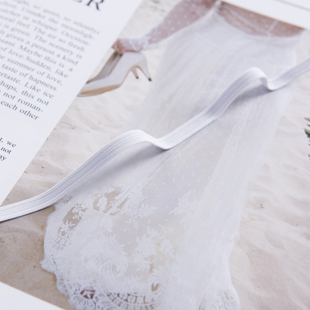White braided elastic band placed on lace apparel fabric