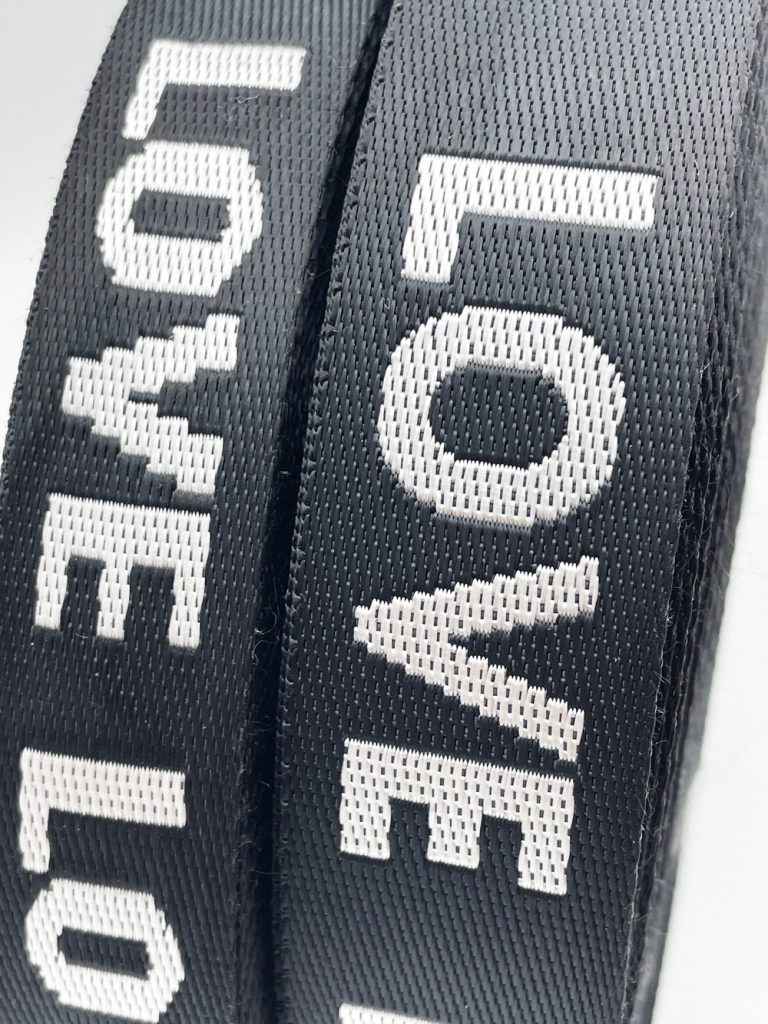 Close-up of black jacquard webbing with white woven lettering showing a dense, even weave structure