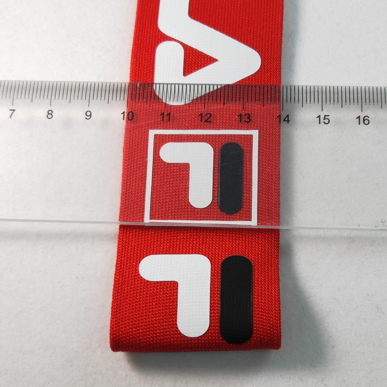 Ruler placed across red printed knitted webbing to show approximate tape width