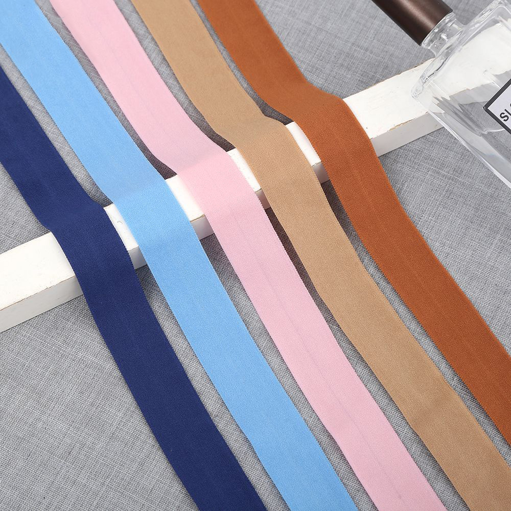 Five elastic binding tapes in navy, light blue, pink, tan and rust brown laid diagonally across a gray fabric surface