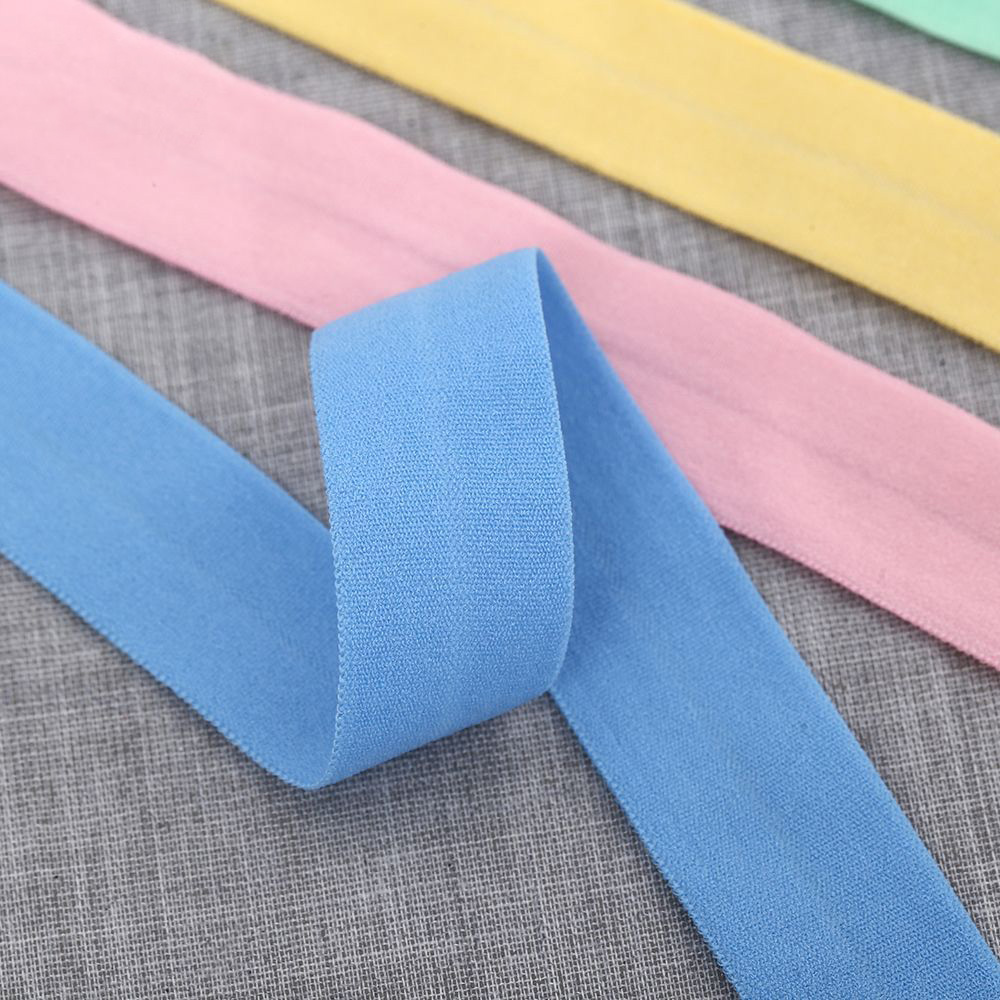 A folded sky blue elastic binding tape showing its fine knit texture, with pink and yellow tapes in the background